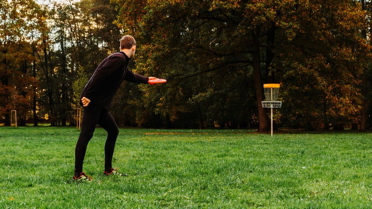 A person throwing a disc golf disc with a disc golf target in the background