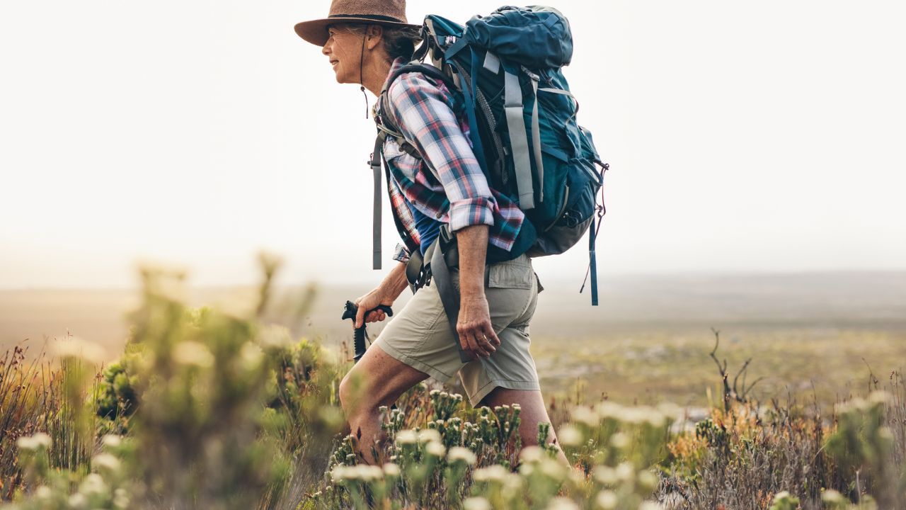 A picture of a person wearing appropriate summer hiking clothes for the trail, including boots, a hat, a backpack, and sunglasses, as recommended for what to wear hiking.