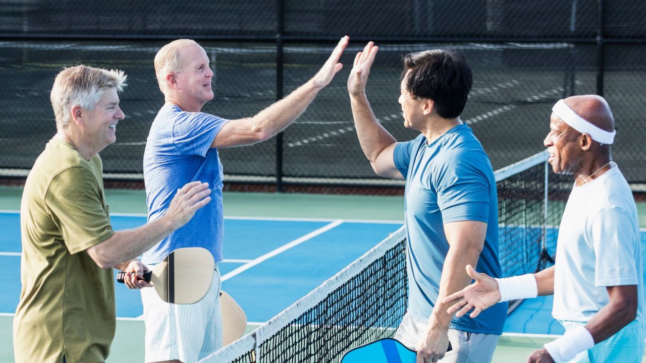 4 people playing pickleball on a court with a net in the middle showing sportmanship