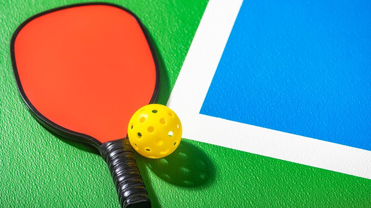 A pickleball paddle and a pickleball ball on a pickleball court