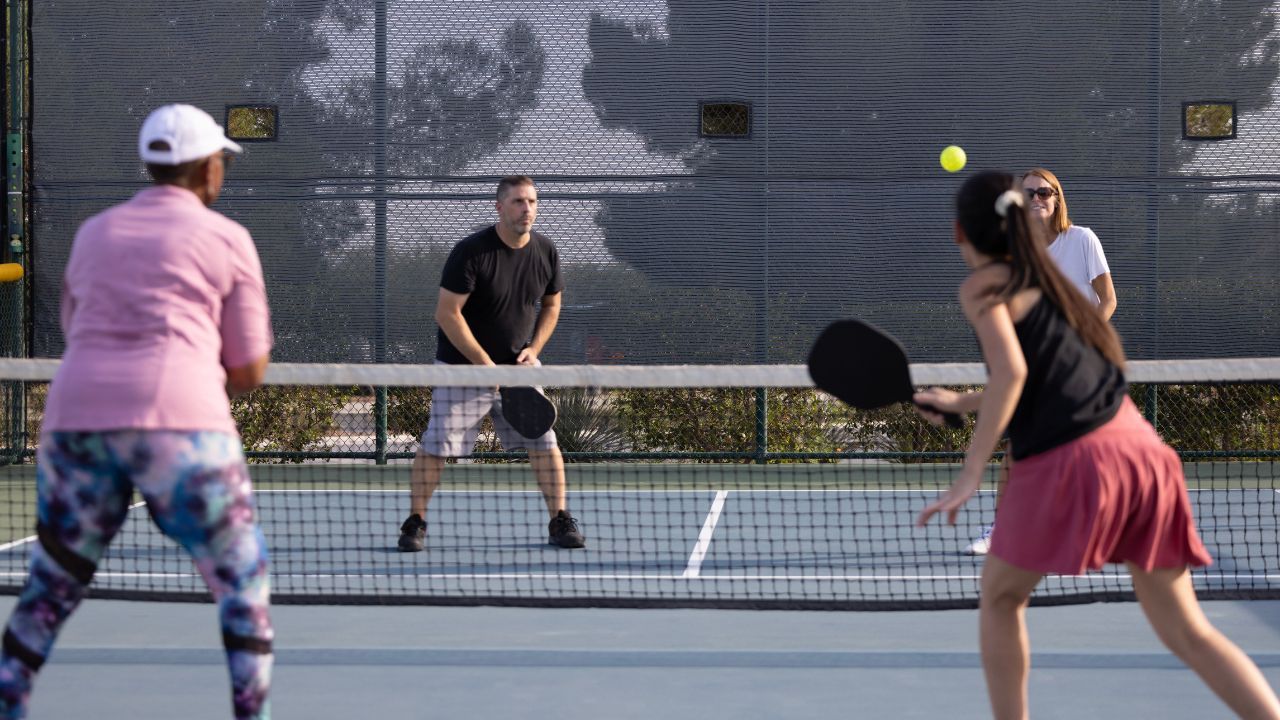 An image showing a group of people playing pickleball, a popular racquet sport that combines elements of tennis, badminton, and ping-pong, used for illustrating what is pickleball and its health benefits and risks.