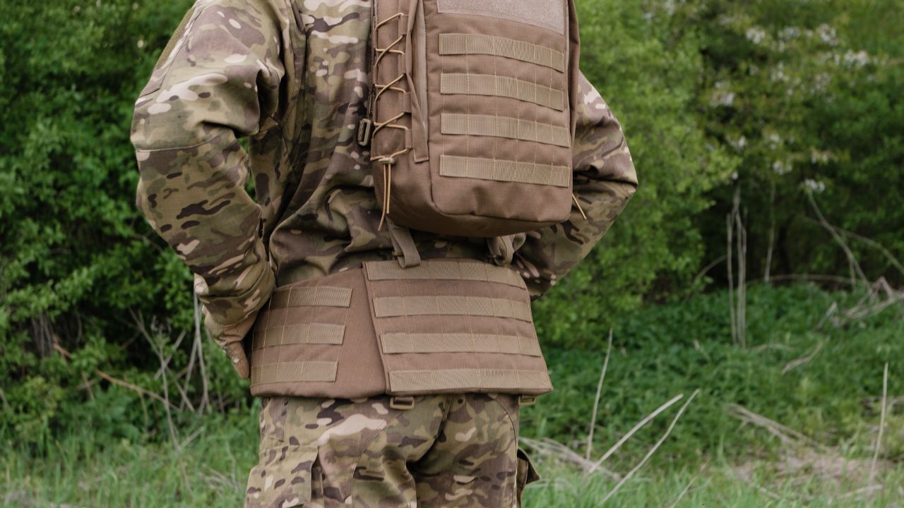 A person wearing tactical gear with a plate carrier and other accessories